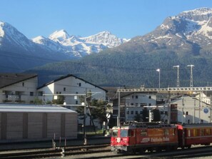 A train station with a mountainous backdrop, featuring a red train labeled "Rheinebene Bahn". - La Residenza 1 by Interhome (Samedan)