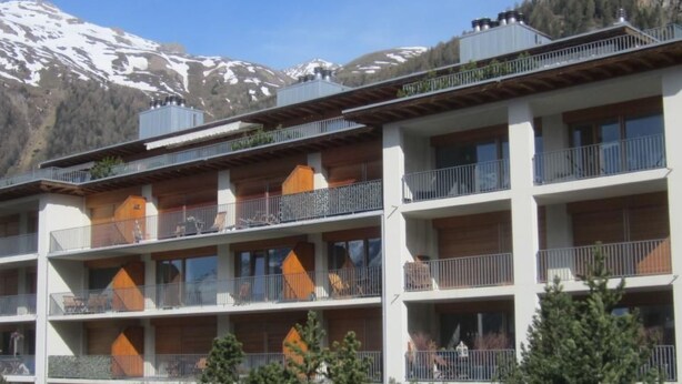 Hotel com vários andares, varandas e montanhas ao fundo.