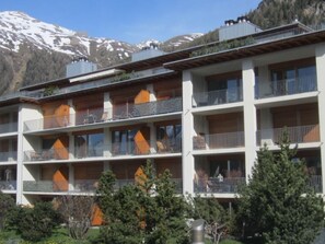Un hotel de varios pisos con balcones y montañas al fondo.