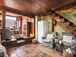 Un salon chaleureux avec une cheminée, deux canapés gris ornés de coussins, une petite table avec une bougie et un escalier.