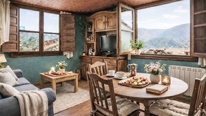 Un cuarto acogedor con techo de madera, una mesa de comedor con sillas, un sofá, una televisión y vistas a montañas a través de amplios ventanales.