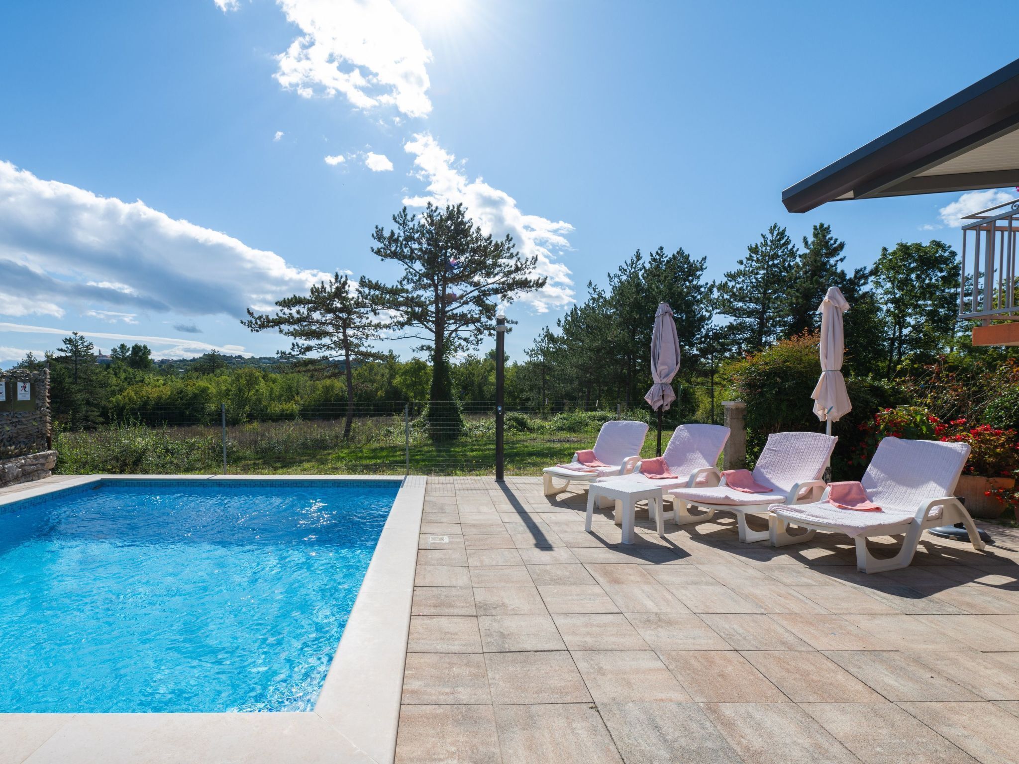 A swimming pool with lounge chairs and umbrellas, surrounded by greenery and a clear sky.