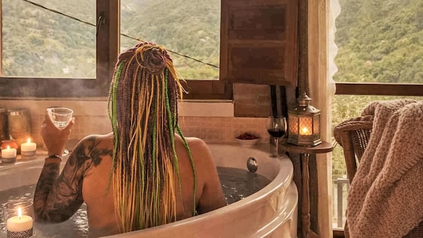 En person i en jacuzzi med udsigt til bjerge, stearinlys og en lanterne.