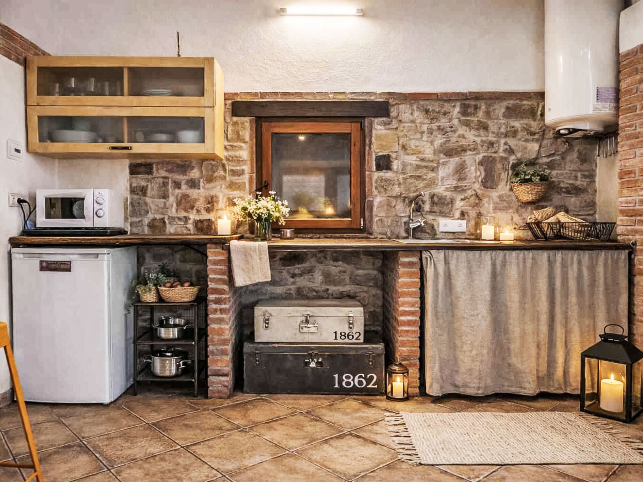 Eine Küche mit Steinwand, Holzschrank, Mikrowelle, Kühlschrank, einem alten Herd und einer Laterne.