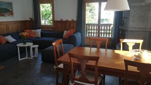 Uma sala de estar com sofá, mesa de jantar com cadeiras, uma mesinha lateral e uma luminária.