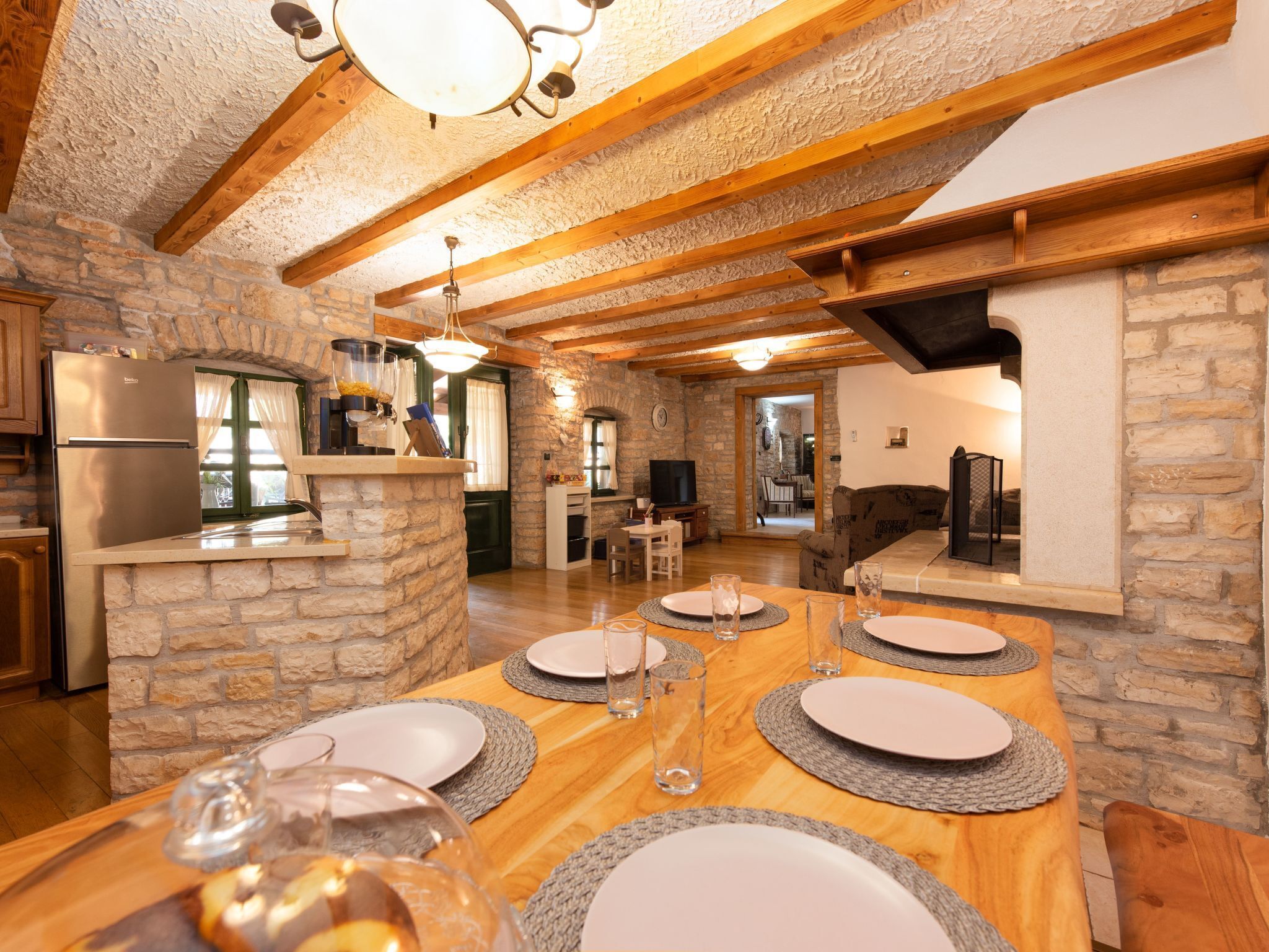 A rustic kitchen with stone walls, wooden beams, and a dining area with a wooden table set for four.