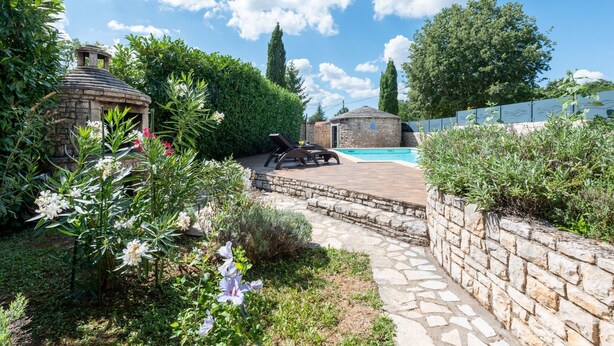 Ein Steingrundbecken, umgeben von einem Garten mit verschiedenen Pflanzen und einer Steinmauer.