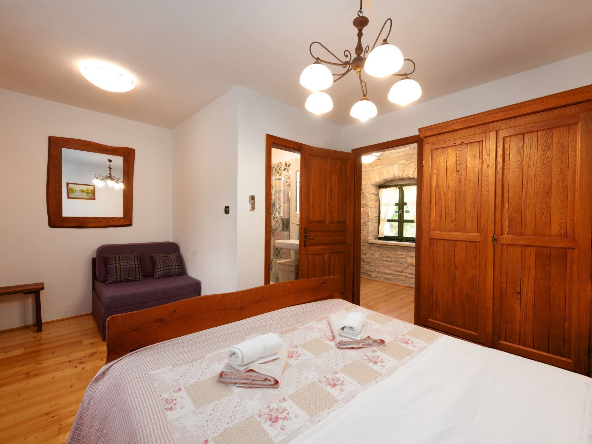 A bedroom with a wooden bed, a purple sofa, a wooden wardrobe, and a mirror on the wall.