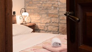 Ein Schlafzimmer mit Stewand, einem Bett mit rosa-weißer Karodecke, einem weißen Handtuch und einem Nachttisch mit Lampe und Wecker.