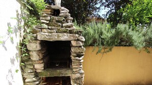 A stone-built outdoor fireplace with logs stored inside, surrounded by greenery and a yellow wall. - Nette Ferienwohnung in Rovinj mit Offenem Kamin by Interhome (Rovinj)