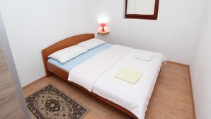 A neatly made bed with white linens and a light blue bedspread, a small rug, a wall-mounted lamp, and a window with curtains. - Nette Ferienwohnung in Rovinj mit Offenem Kamin by Interhome (Rovinj)