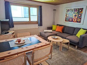 Ein Wohnzimmer mit einer Couch, einem Esstisch, Stühlen, einem Fernseher, einer Heizung und einem Gemälde.