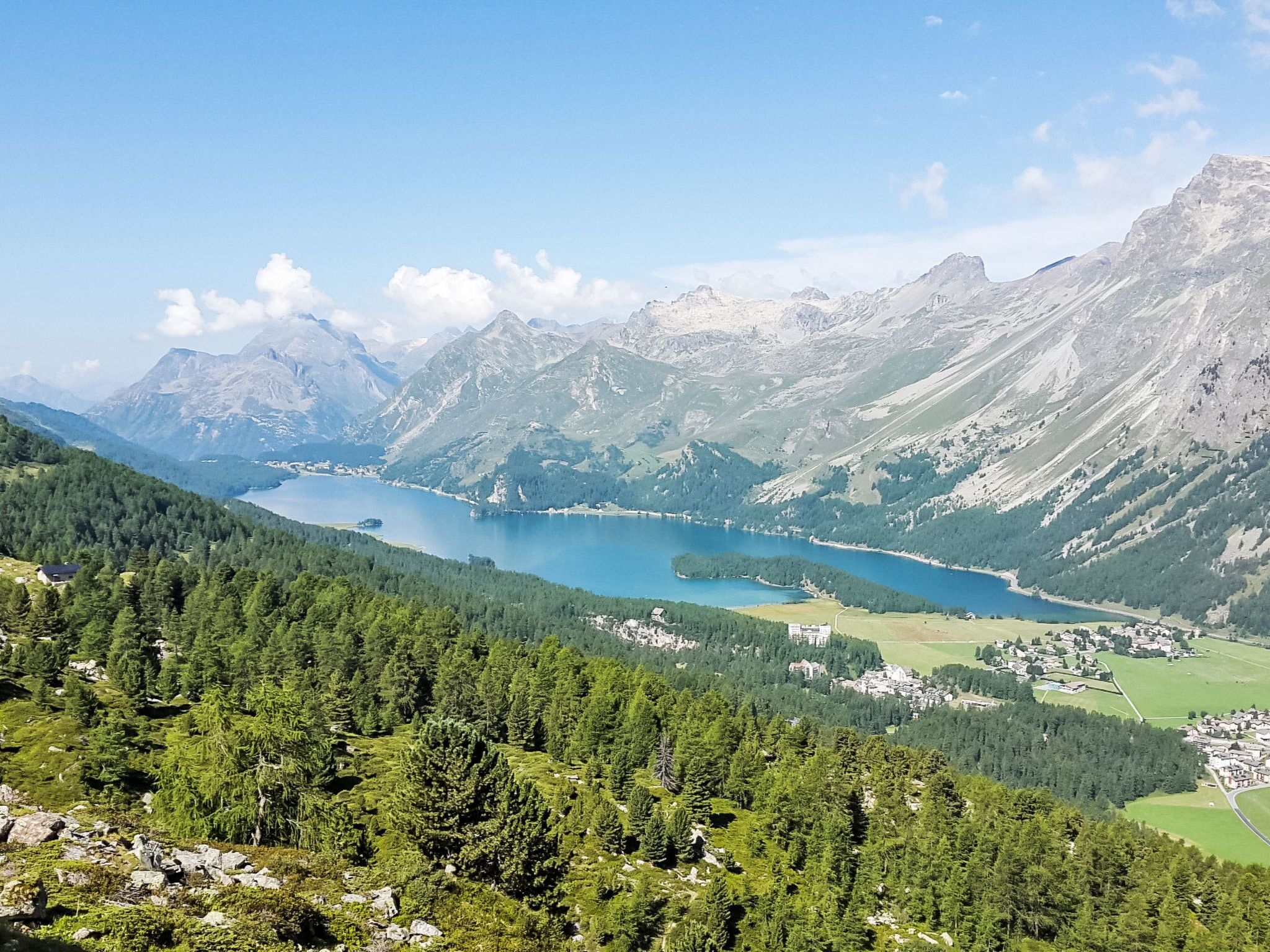 Eine gebirgige Landschaft mit einem See, dichten Wäldern und einer kleinen Siedlung.