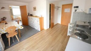 Cocina compacta con estufa, comedor con mesa y sillas, y pequeña zona de kitchenette.