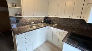 Eine kompakte Küche mit weißen Schränken, Granit Arbeitsplatten, einem Edelstahl-Spülbecken und einem eingebauten Herd.