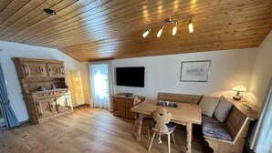 Ein Wohnbereich mit Holzboden, einem Esstisch, einer Couch und einem an der Wand befestigten Fernseher.
