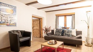 A living room with a wooden floor, a sofa, a chair, a coffee table, and a poster on the wall. - Chesa Treig by Interhome (Samedan)