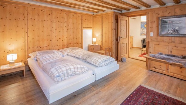 A wooden-paneled room with a bed, bedside tables, a rug, and a painting. - Chesa Treig by Interhome (Samedan)