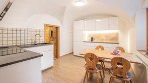 A modern kitchen with white cabinets, a wooden dining table, and two wooden chairs. - Chesa Treig by Interhome (Samedan)