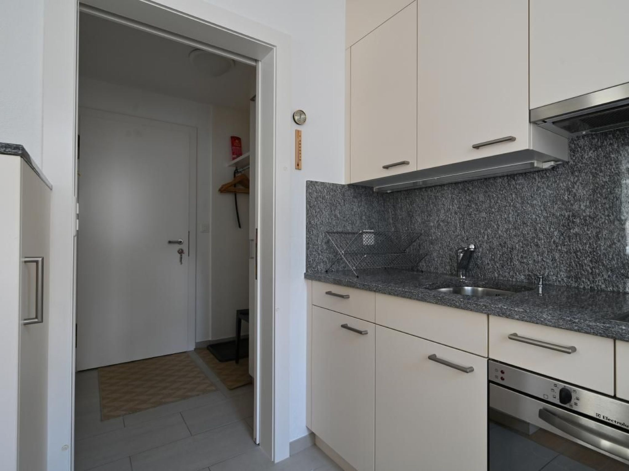 Une cuisine moderne avec des meubles blancs, un plan de travail en granit, un évier en acier inoxydable et un lave-vaisselle Electrolux.
