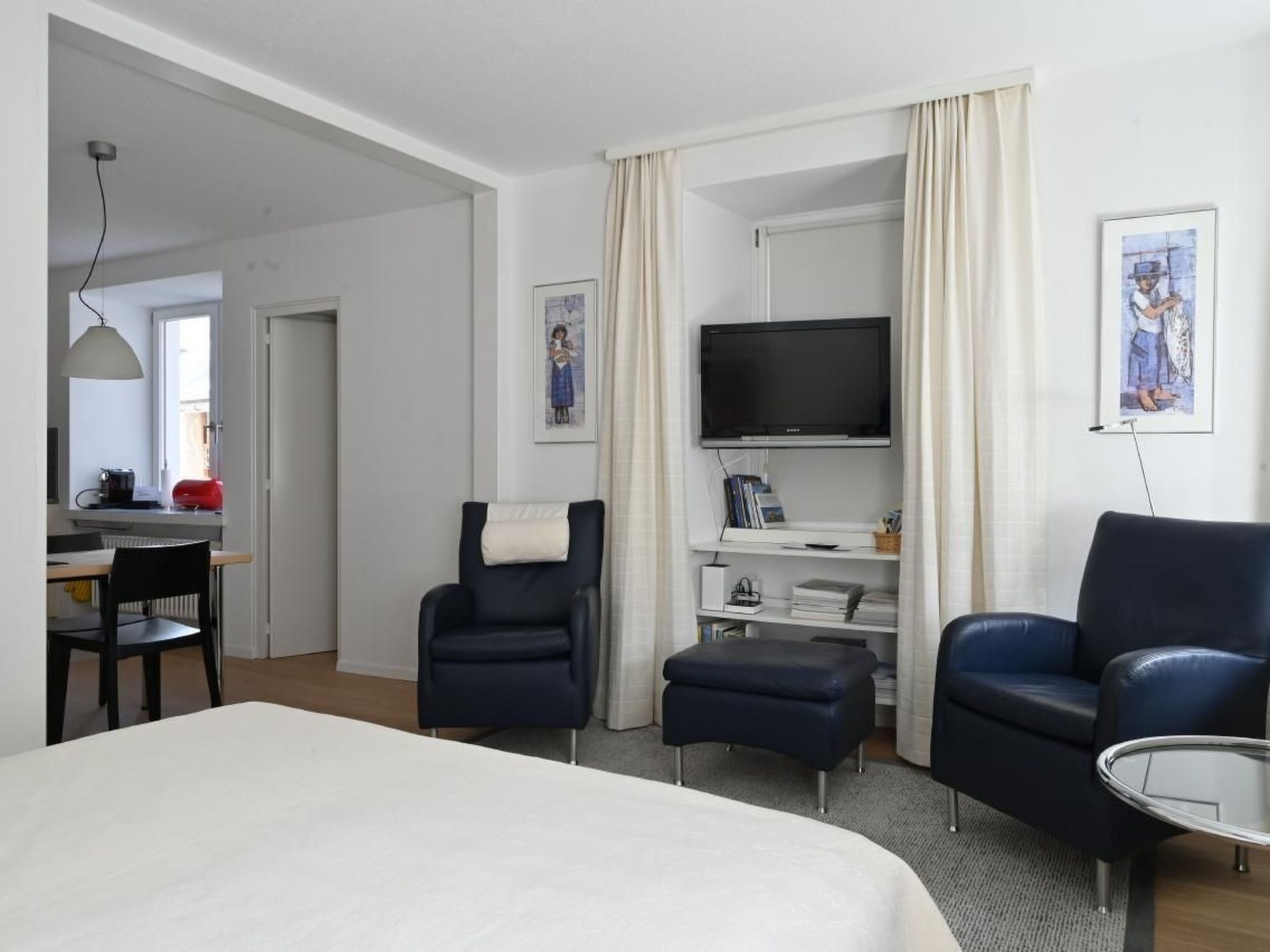 Une chambre d’hôtel comprenant un lit, deux fauteuils, un téléviseur, un bureau avec une lampe et une fenêtre.