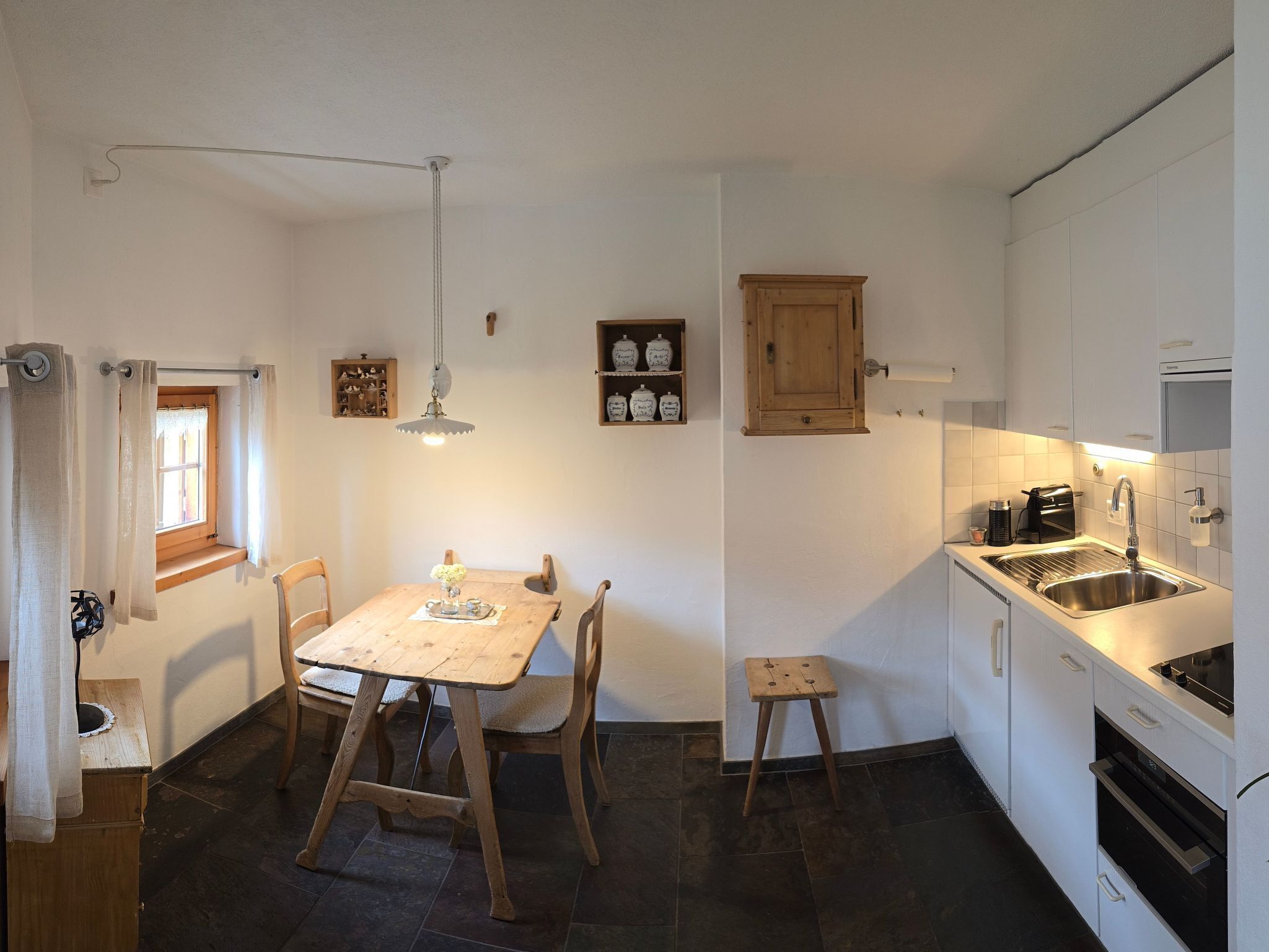 Eine kleine Küche mit Holztisch und -stühlen, einem Hocker, einer Pendelleuchte und einem Holzschrank über der Spüle.