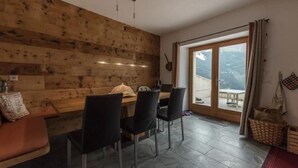 A dining area with a wooden wall, a table with chairs, and a view through a glass door. - Monte Campell Dasura by Interhome (Poschiavo)