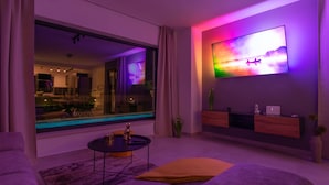Una sala de estar moderna con un ventanal grande, un televisor de pantalla plana montado en la pared, un sofá, una mesa de centro y una mesita auxiliar.