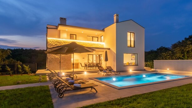Una casa moderna de dos pisos con piscina, muebles de exterior y fachada de piedra.