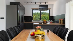 Una cocina moderna con una isla grande, sillas negras y una mesa de comedor con frutas y un florero.