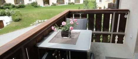 Un balcon avec une table et des chaises, un pot de fleurs orné de fleurs roses et une vue sur un immeuble doté de balcons.