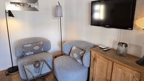 Uma sala de estar aconchegante com um sofá, uma mesa de centro de vidro, uma televisão, um abajur e um armário de madeira.