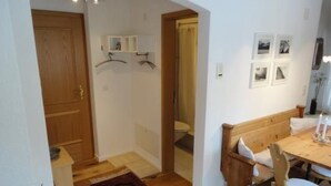 Quarto com porta de madeira, um banco, uma mesa com cadeiras e parede com quadros.