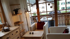 Une pièce chaleureuse avec une table en bois, un canapé blanc et une fenêtre donnant sur des immeubles et des voitures.