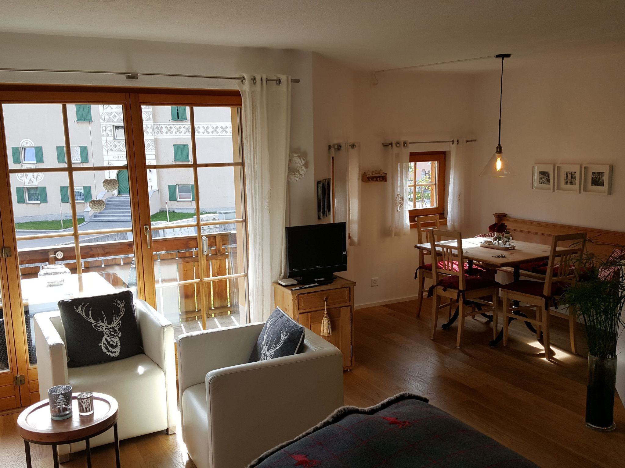 Ein gemütliches Wohnzimmer mit einer Couch, einem Fernseher, einem Esstisch mit Stühlen und Blick ins Freie.