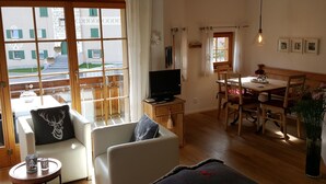 Un salon confortable avec un canapé, un téléviseur, une table à manger avec des chaises et une vue sur l’extérieur.
