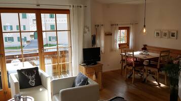 Ein gemütliches Wohnzimmer mit einer Couch, einem Fernseher, einem Esstisch mit Stühlen und Blick ins Freie.
