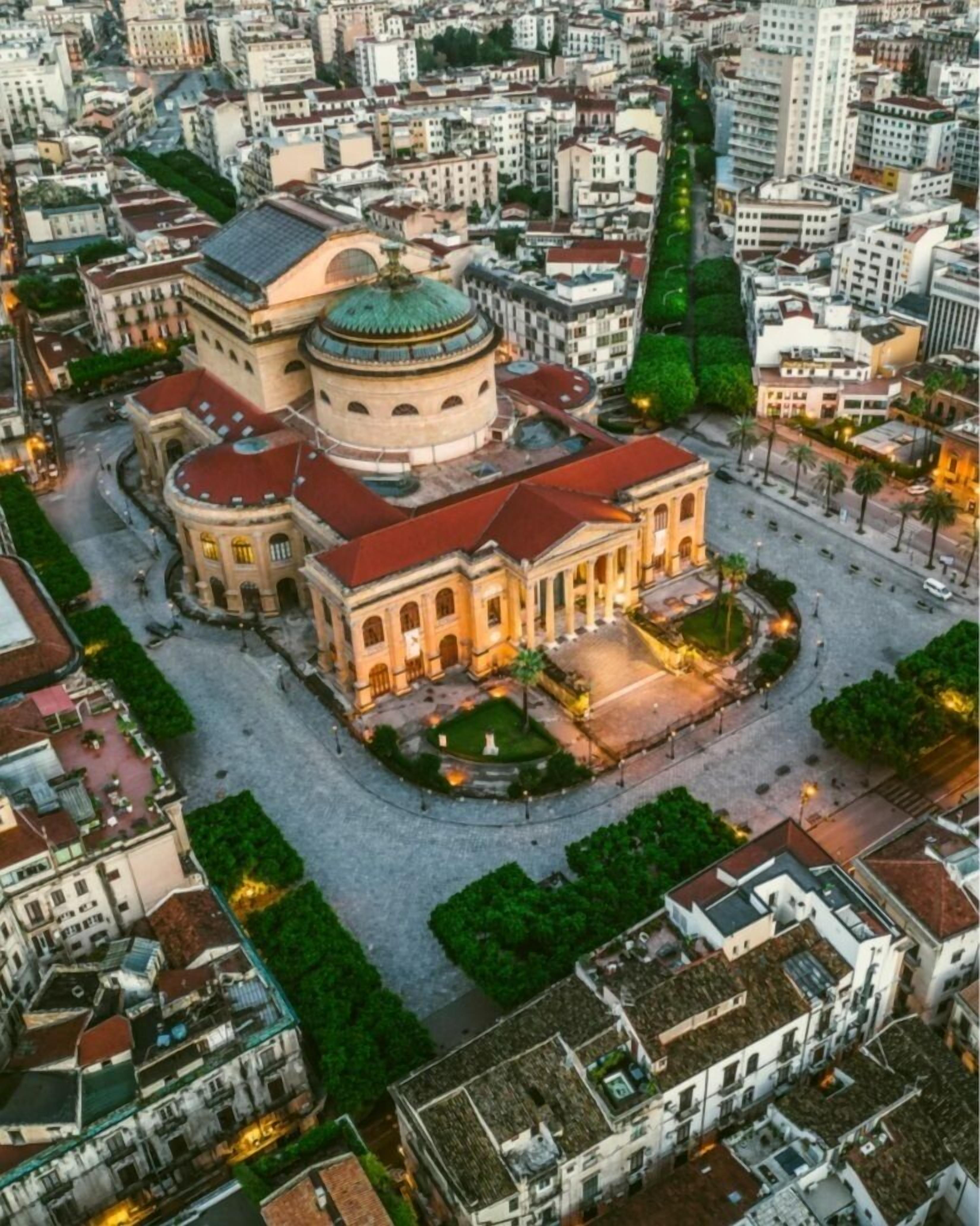 An aerial view of a historic building with a central dome, surrounded by a square courtyard with trees and a fountain.
