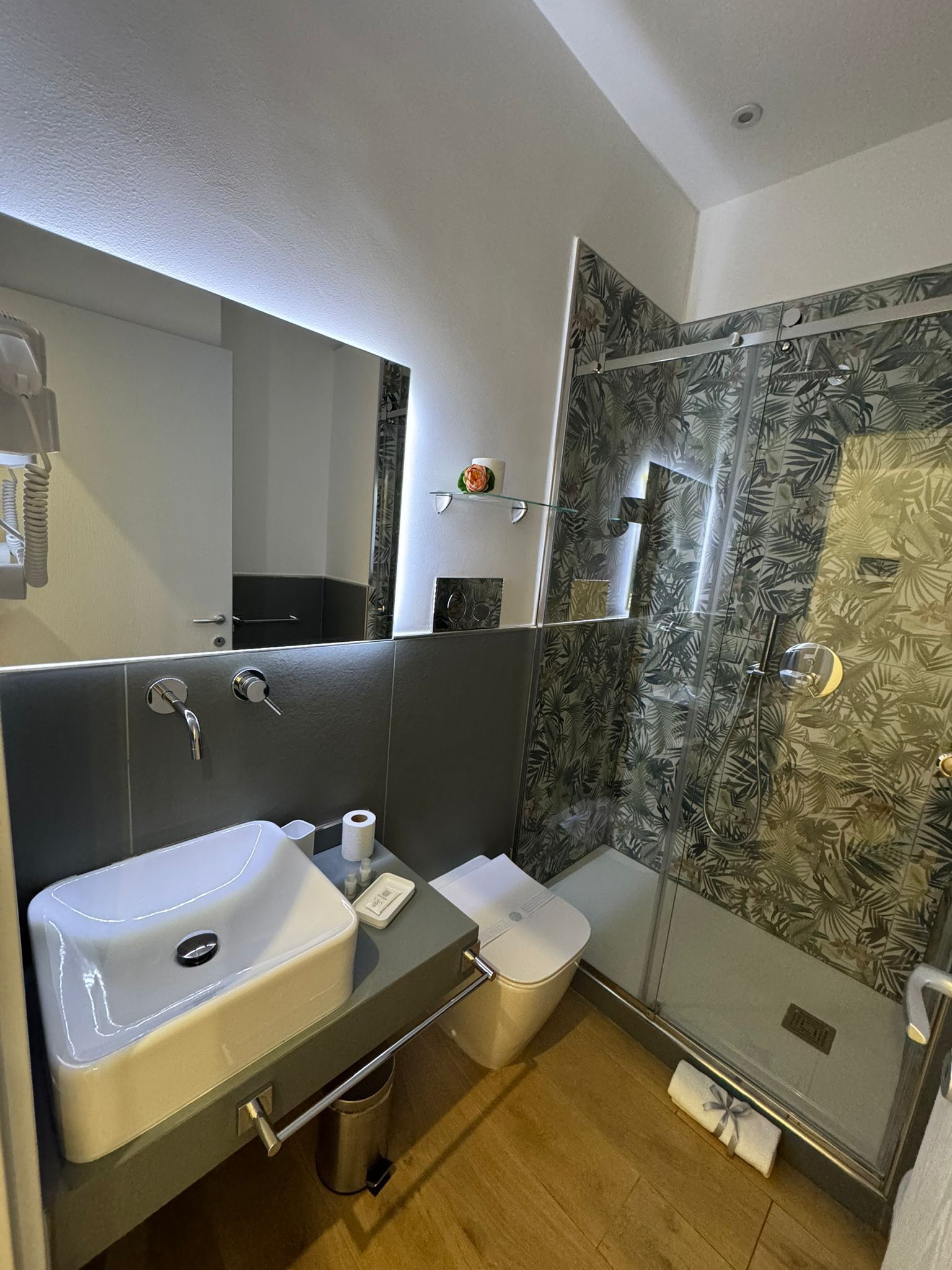 A modern bathroom with a large mirror, a sink, a toilet, and a shower area.