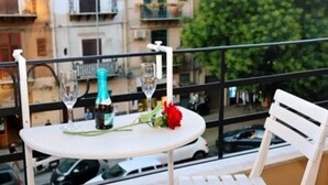 A balcony with a round table, two wine glasses, a bottle, and a red flower. - B&B Central Station  (Palermo)