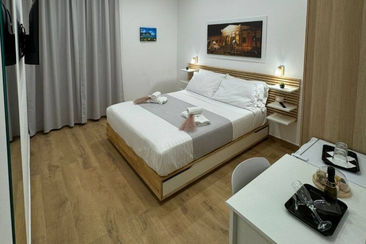 A hotel room with a bed, bedside tables, a desk, and a TV.