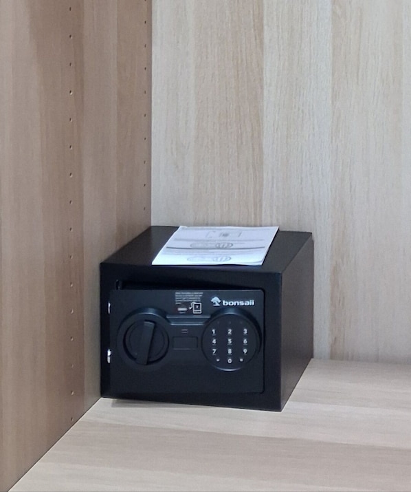 Um cofre preto com teclado e um papel em cima, encostado em uma parede de madeira.
