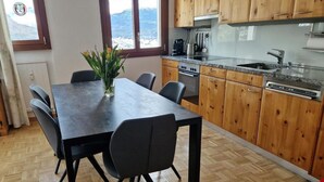 Cozinha moderna com armários de madeira, bancada de granito e área de refeições com mesa e cadeiras escuras.