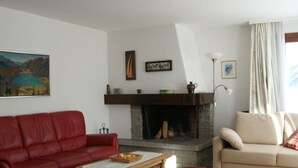 Uma sala de estar com lareira, sofá de couro vermelho, sofá bege e uma pintura na parede.