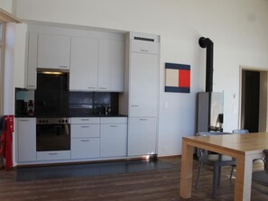 A modern kitchen with white cabinets, a black stove, and a dining area with a wooden table and chairs. - Sur Puoz 13 by Interhome (Samedan)