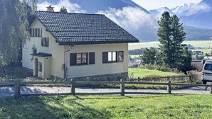 Een huis met twee verdiepingen, een schuin dak, een klein terras en een houten hek ervoor.