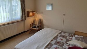 Une chambre à coucher comprenant un lit, une chaise, une fenêtre avec des rideaux, un radiateur et un luminaire fixé au mur.