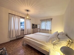 A bedroom with a large bed, a dresser, a radiator, and a window with curtains.
