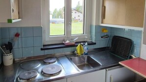 Une cuisine équipée d’un évier à deux bacs, de deux plaques de cuisson, d’une fenêtre donnant sur une maison et de murs recouverts de carreaux bleus.