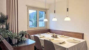 Een eethoek met een tafel voor vier personen, een houten bank en een raam met uitzicht op een berg.
